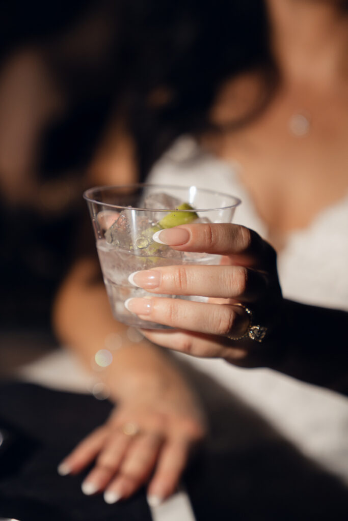 Bride holding cocktail with lime during wedding reception.