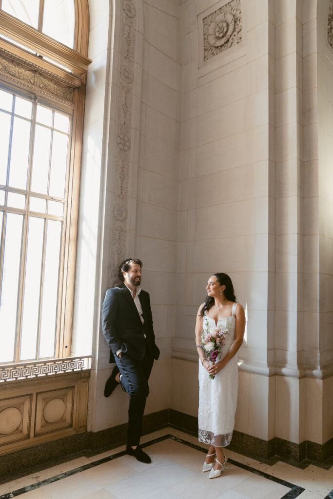 Bride and groom posing by tall windows at Valentine’s Day wedding courthouse.