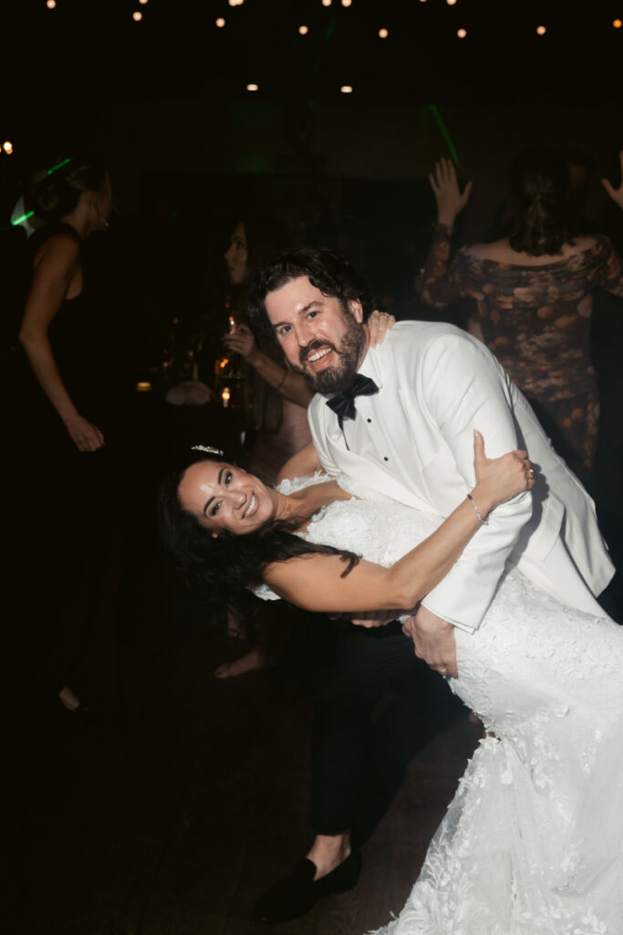 Bride smiling as groom dips her on the dance floor during reception celebration.