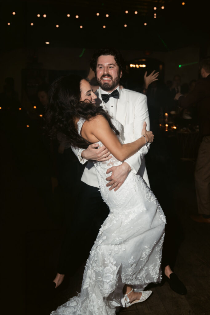 Bride and groom hugging on crowded dance floor at night.