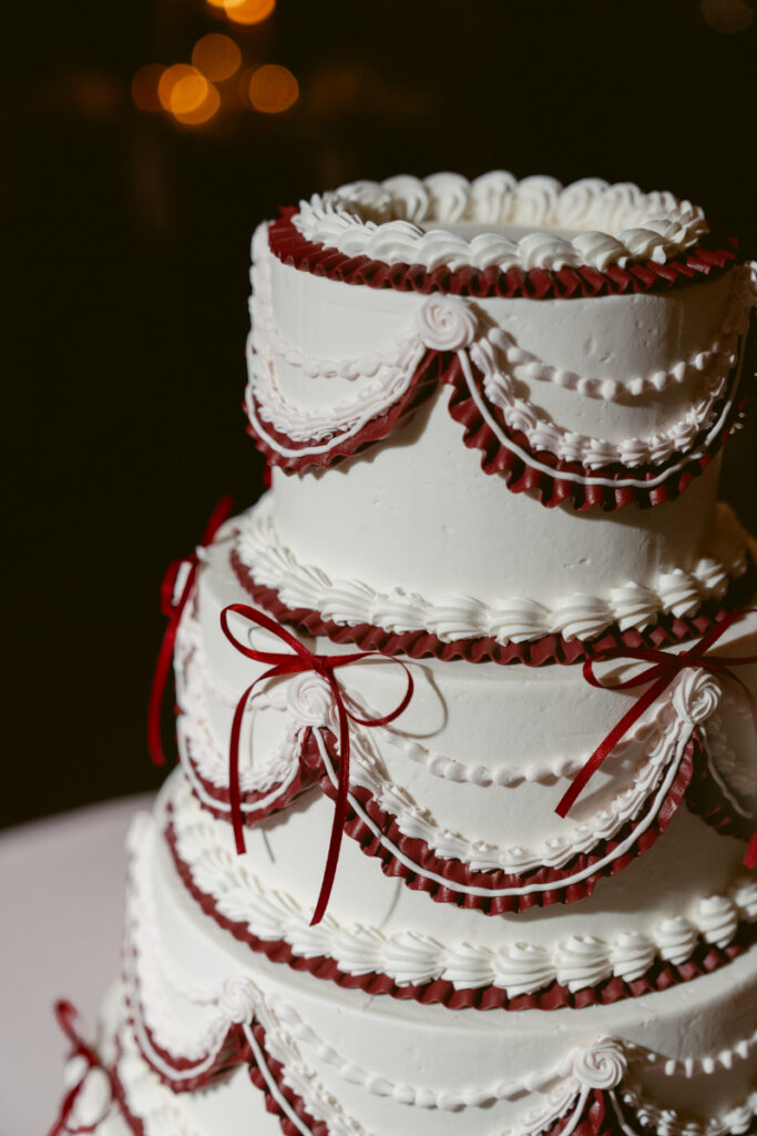 Elegant white wedding cake with red bows and layered piping detail.