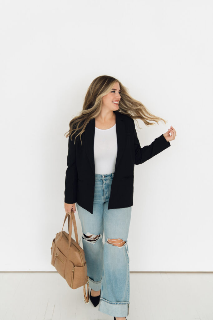Professional branding photography of woman in blazer and jeans with tan bag, smiling confidently.