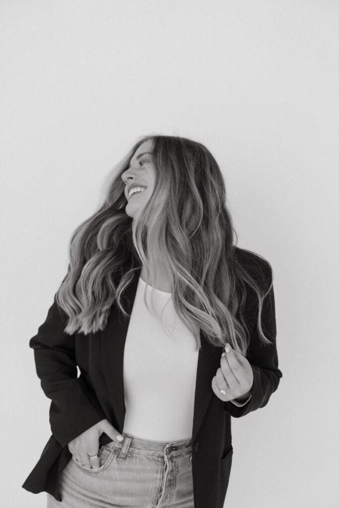 Black and white portrait of smiling woman in blazer, looking away with flowing hair.