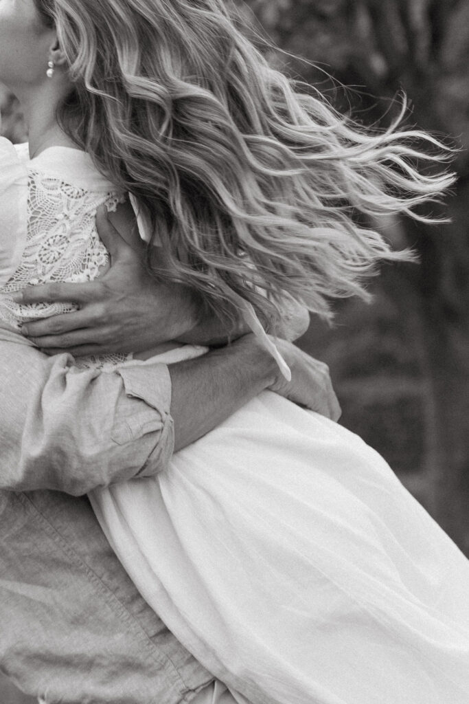 A close-up black-and-white shot captures flowing hair and an embrace, focusing on texture and movement. The cropped composition emphasizes intimacy—artistic natural engagement photos with a refined, editorial feel.