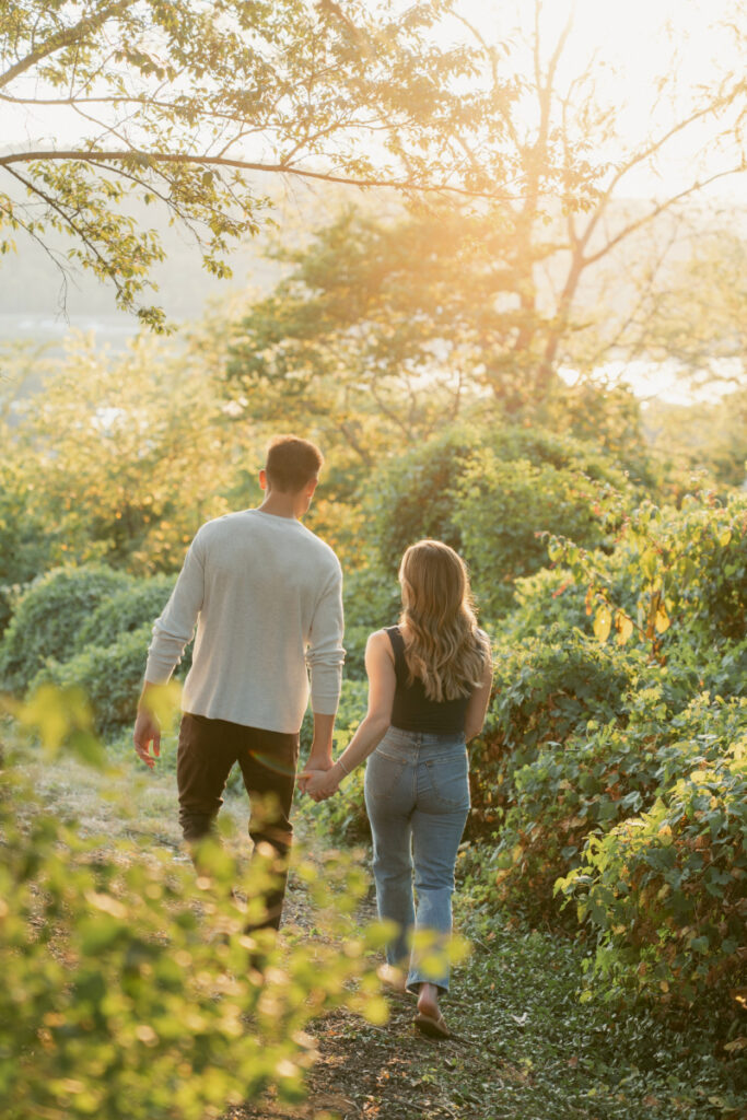 Couple walking hand in hand through sunlit path with warm golden light and lush greenery