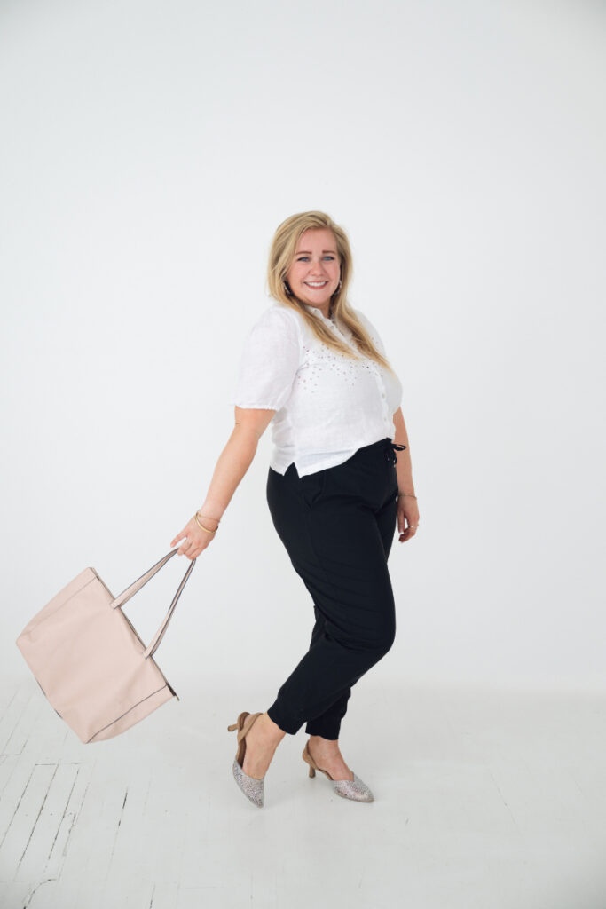 Full length portrait of smiling woman in white blouse and black pants holding handbag.