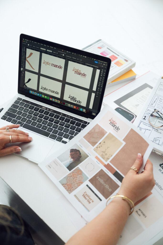 Brand photography image of designer reviewing logo concepts on laptop and print materials.