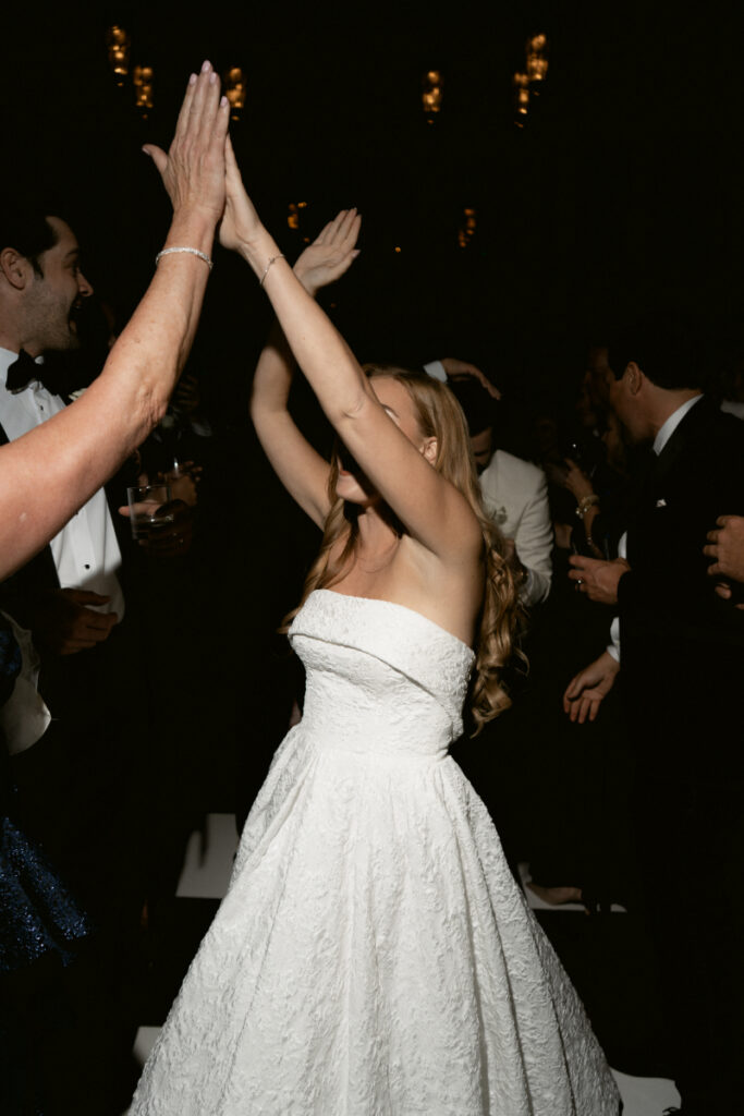 Bride and guests dancing with hands in the air on the dance floor.