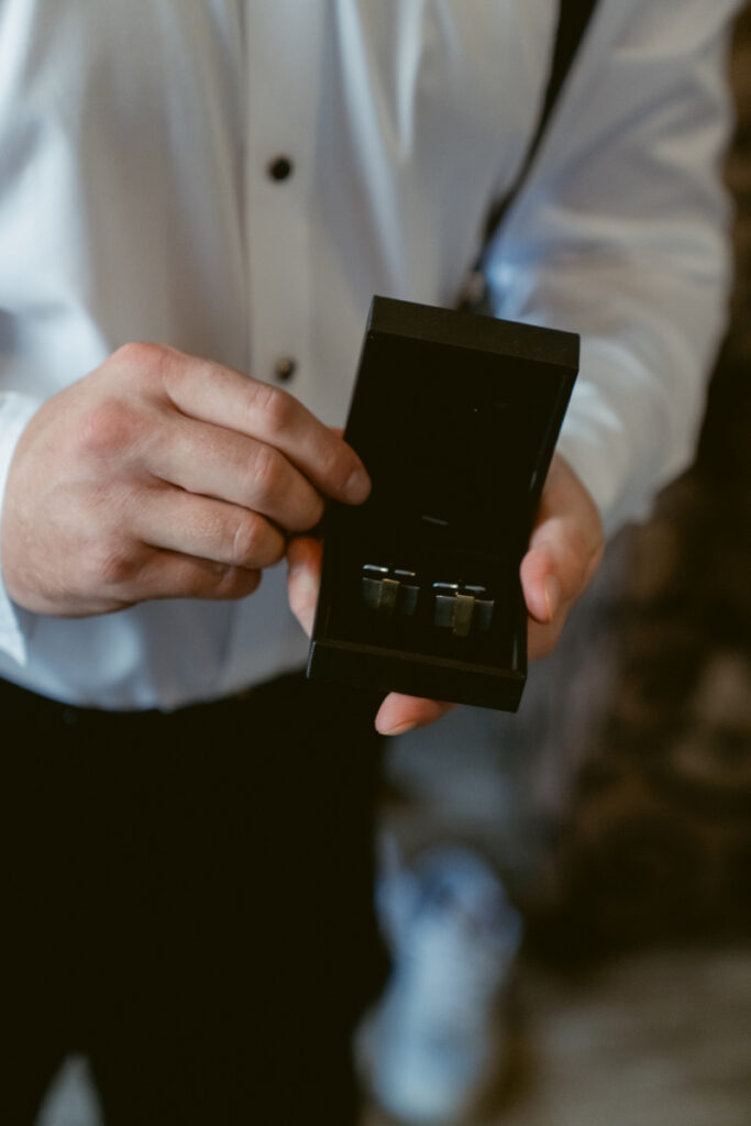 Groom holding cufflinks in a box during getting ready at a Hilton Netherland Plaza wedding.