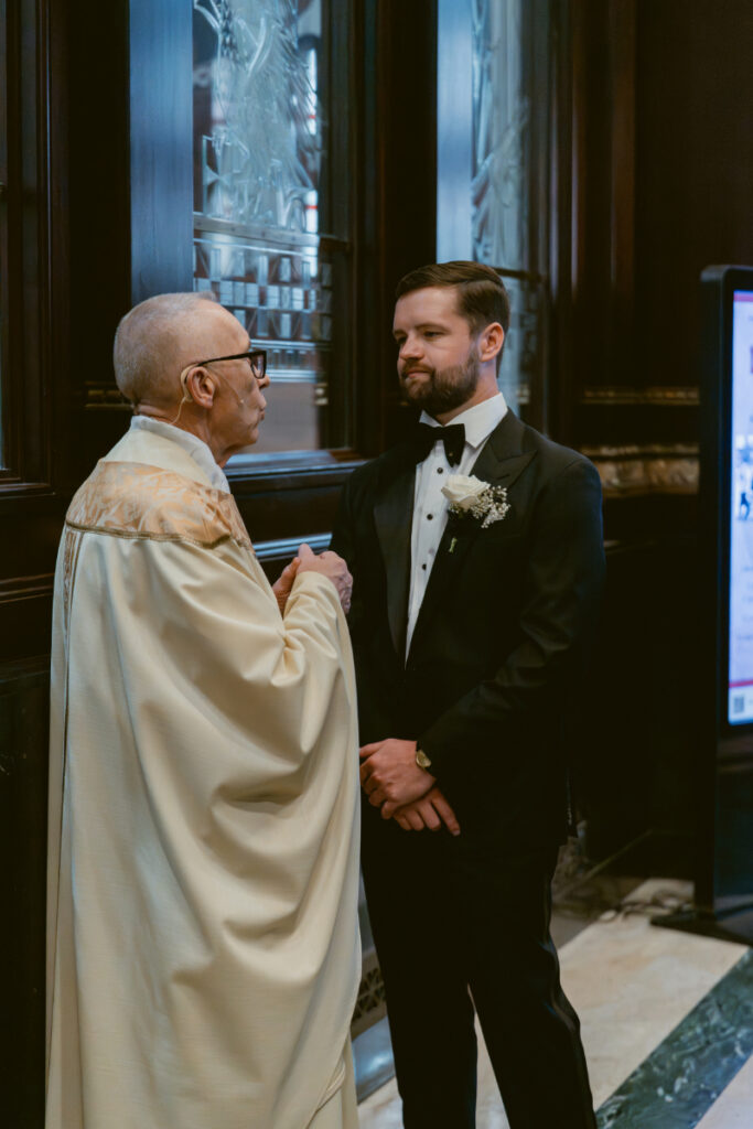 Groom speaking with priest before ceremony at St. Peter in Chains during a Hilton Netherland Plaza wedding.