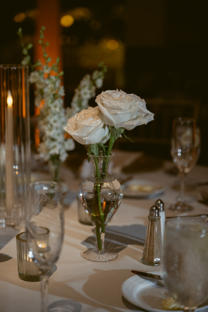 Single white rose centerpiece in a glass vase on a reception table.