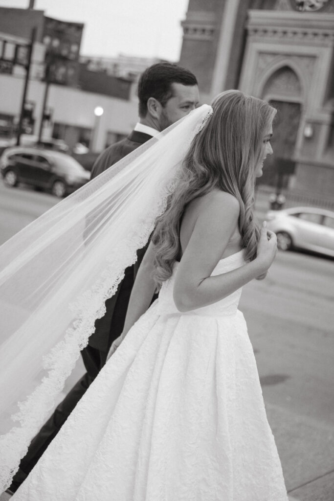 Black and white candid of the bride and groom walking together with veil flowing.