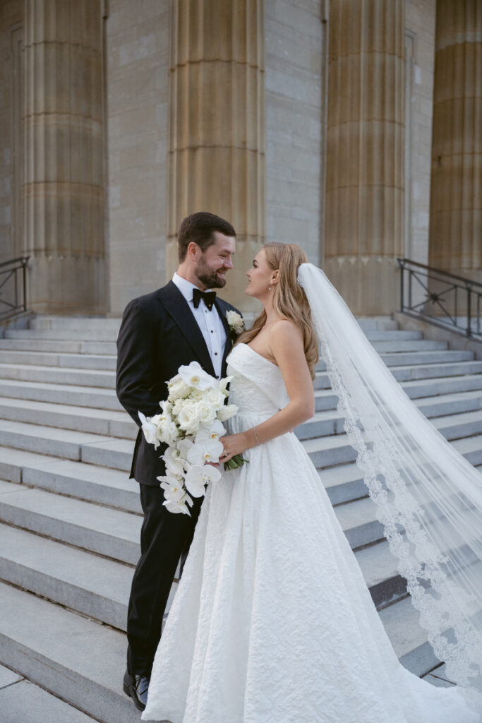 Bride and groom standing together on the steps holding a cascading bouquet.