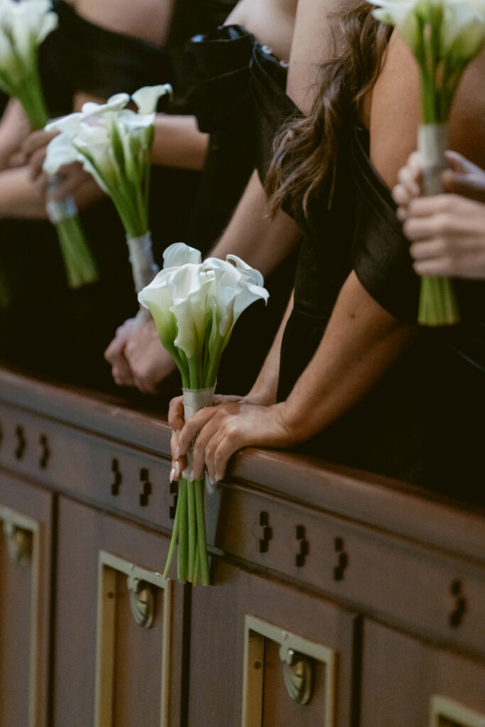 Bridesmaids holding white calla lily bouquets along the aisle.