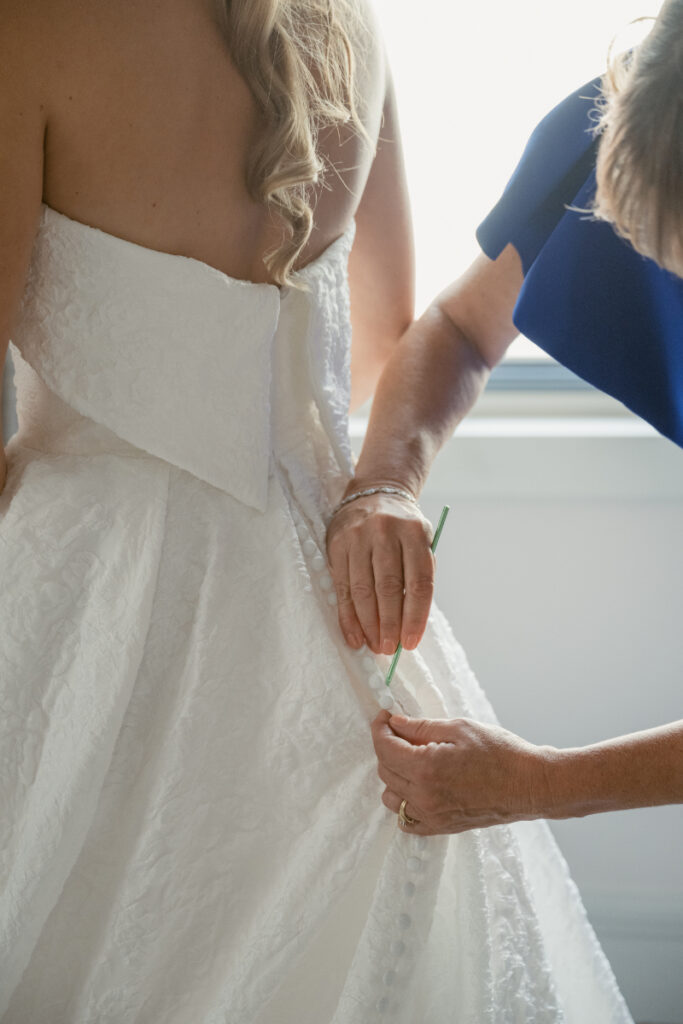 Bride getting into her gown with help during wedding morning at a Hilton Netherland Plaza wedding.