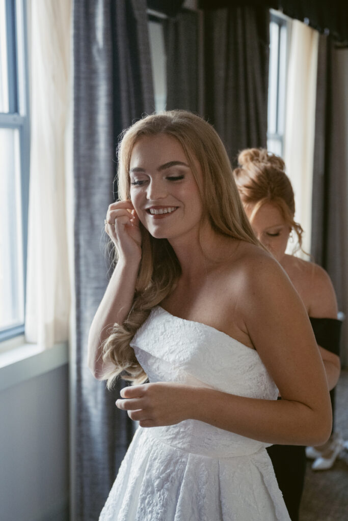 Bride putting on earrings with help during bridal prep at a Hilton Netherland Plaza wedding.