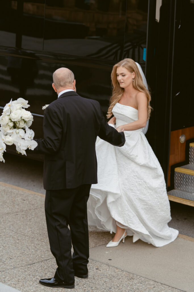 Bride stepping out of a bus with bouquet before ceremony at a Hilton Netherland Plaza wedding.