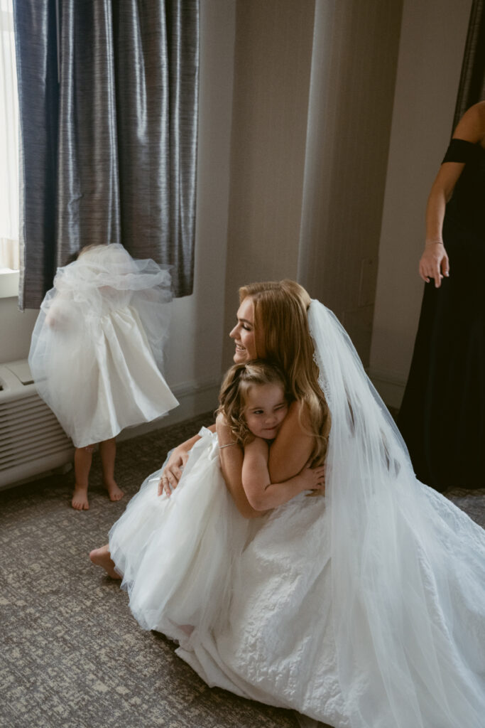 Bride hugging a flower girl during a candid getting ready moment at a Hilton Netherland Plaza wedding.
