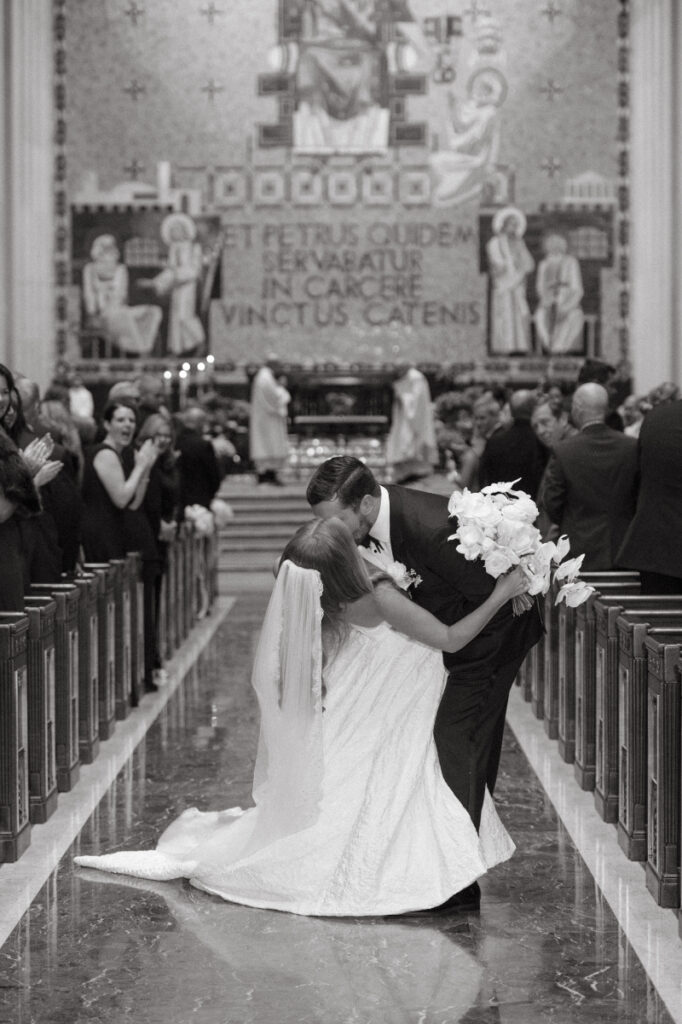 Couple sharing a dip and kiss in the aisle as guests celebrate around them.