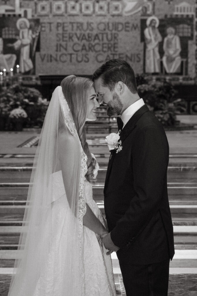 Black and white portrait of the bride and groom smiling with their foreheads touching during the ceremony.