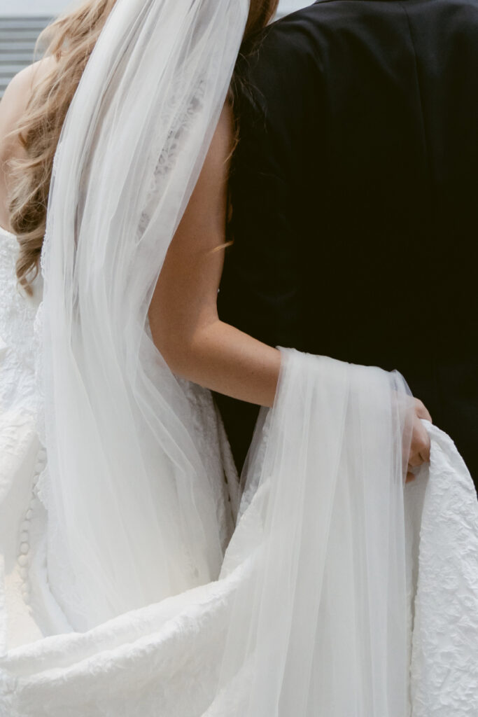 Close-up of the bride’s veil and dress as she holds the fabric.