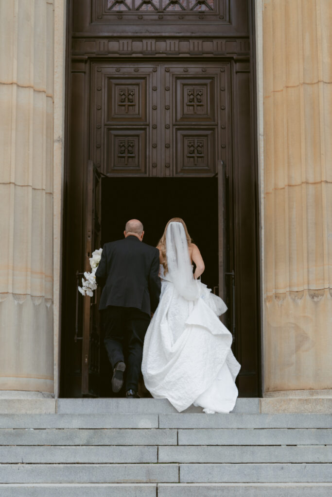Bride and parent walking into St. Peter in Chains Basilica for the ceremony during a Hilton Netherland Plaza wedding.