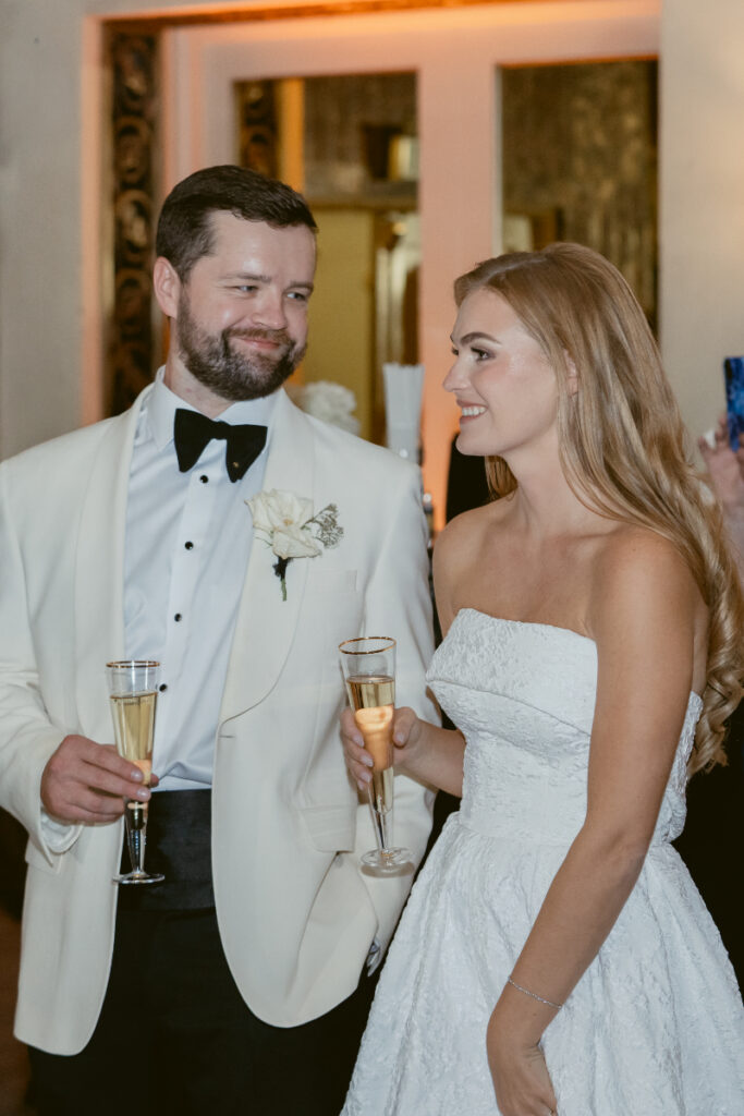 Bride and groom smiling and holding drinks during cocktail hour.