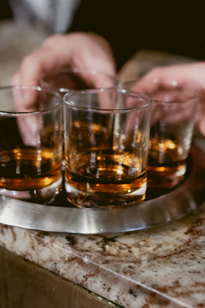 Close-up of whiskey glasses on tray with hands reaching in for a celebratory toast