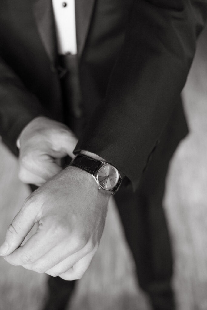 Black and white close-up of groom adjusting watch, wedding checklist for groom detail moment