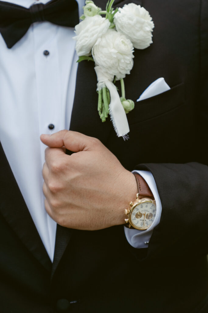 Close-up of groom adjusting jacket with boutonniere and watch, clean and polished wedding look