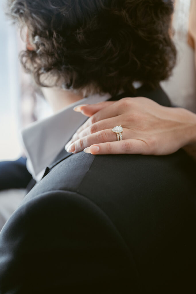 Close-up of bride’s hand with ring resting on groom’s shoulder, wedding checklist for groom moment