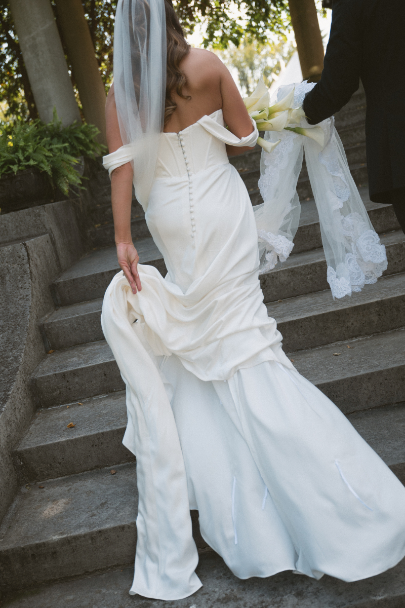 Bride walking up stone steps while carrying her gown, showcasing elegant wedding dress details.
