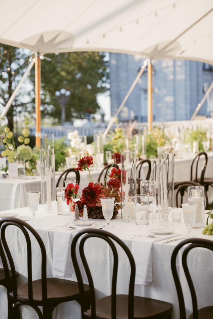 Elegant reception table with deep red florals, glass candleholders, and classic black chairs.