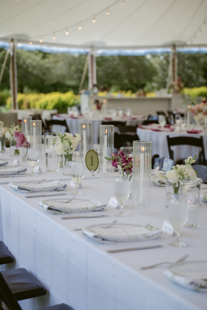 Long reception table set with florals, candles, and place settings beneath the tent.