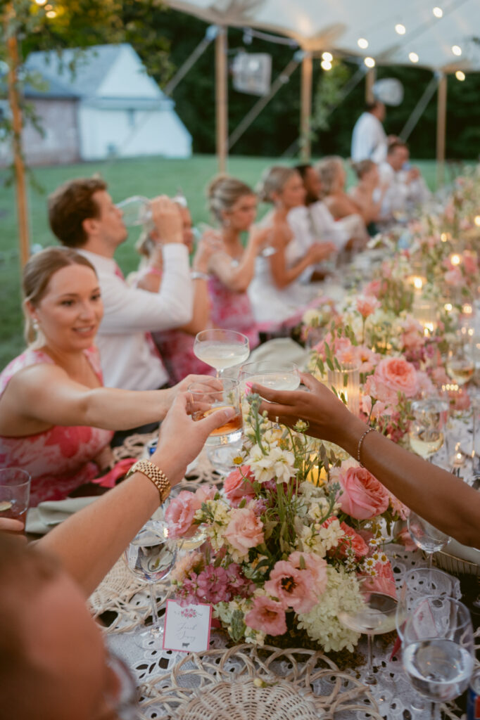 Wedding guests toast during an outdoor reception with colorful flowers and candlelit tables.