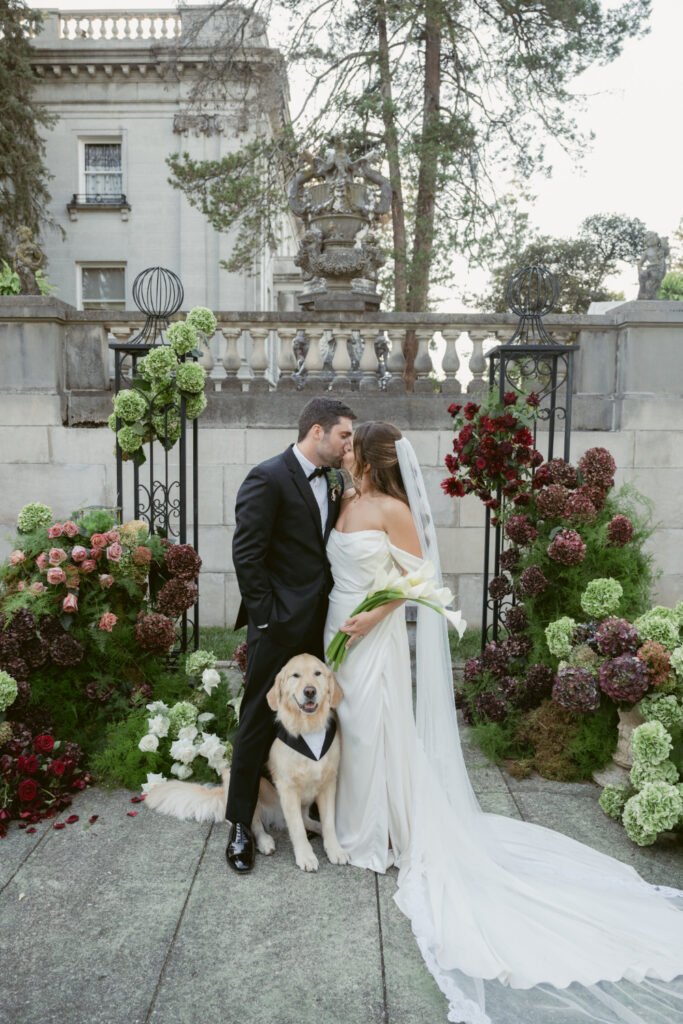 Bride and groom kiss among lush flowers at one of Cincinnati's elegant garden wedding venues with their dog.