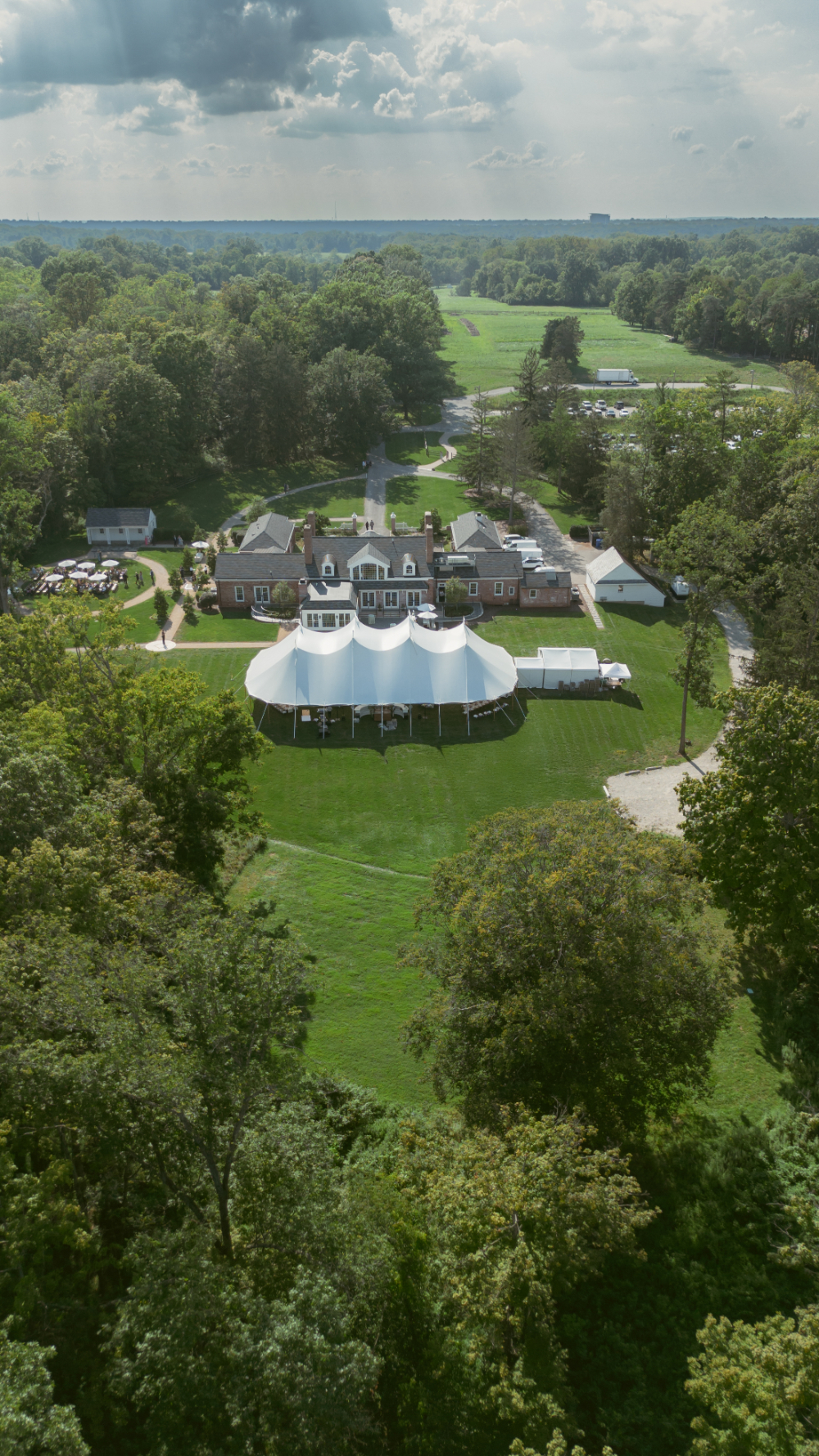 Aerial view of a countryside wedding venue with white tents, green lawns, and surrounding trees.