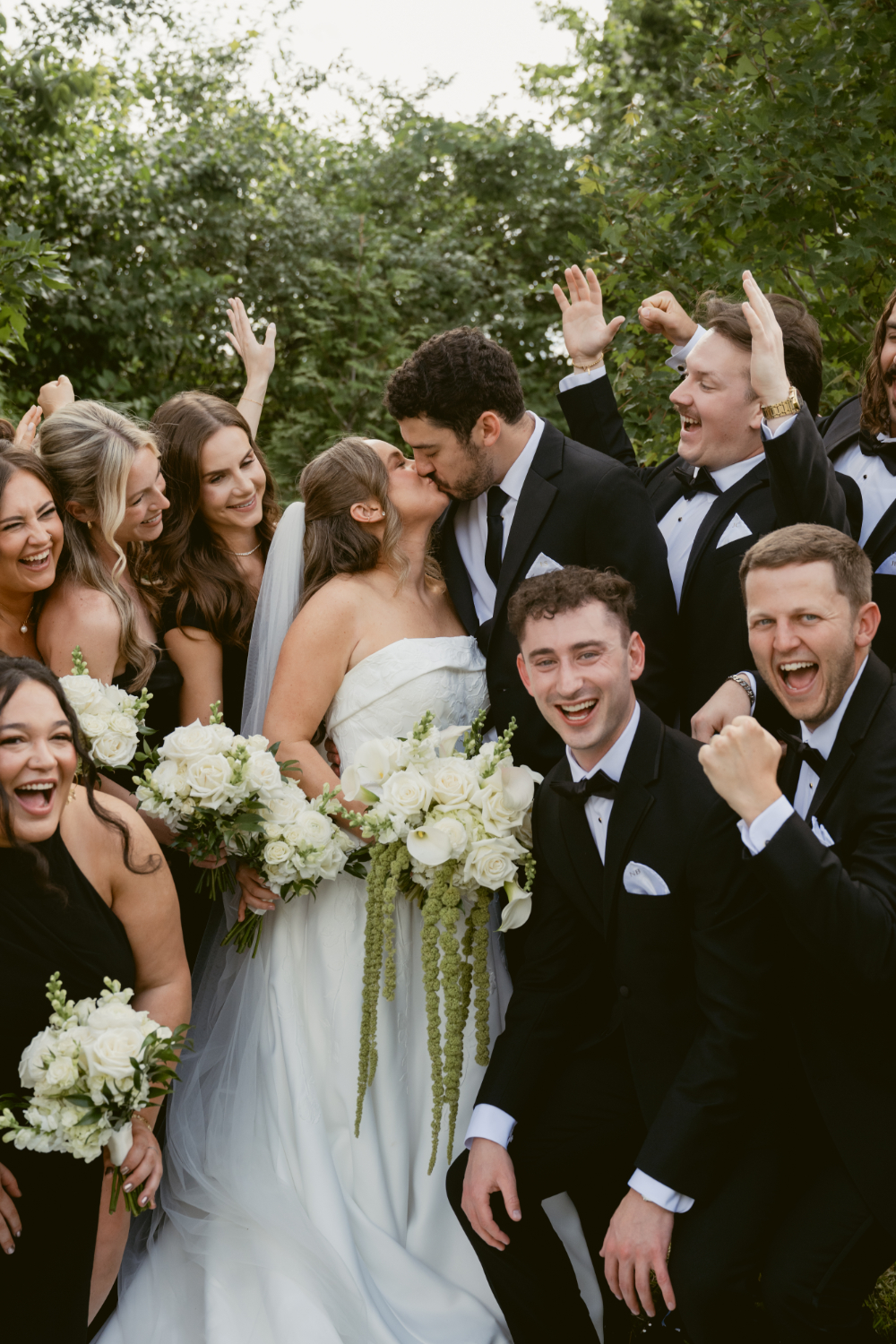 Bride and groom kissing while their wedding party cheers and celebrates around them.